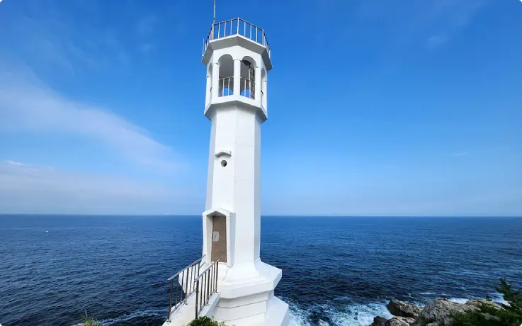 White Big End Lighthouse standing on rocky coastline with blue sea background