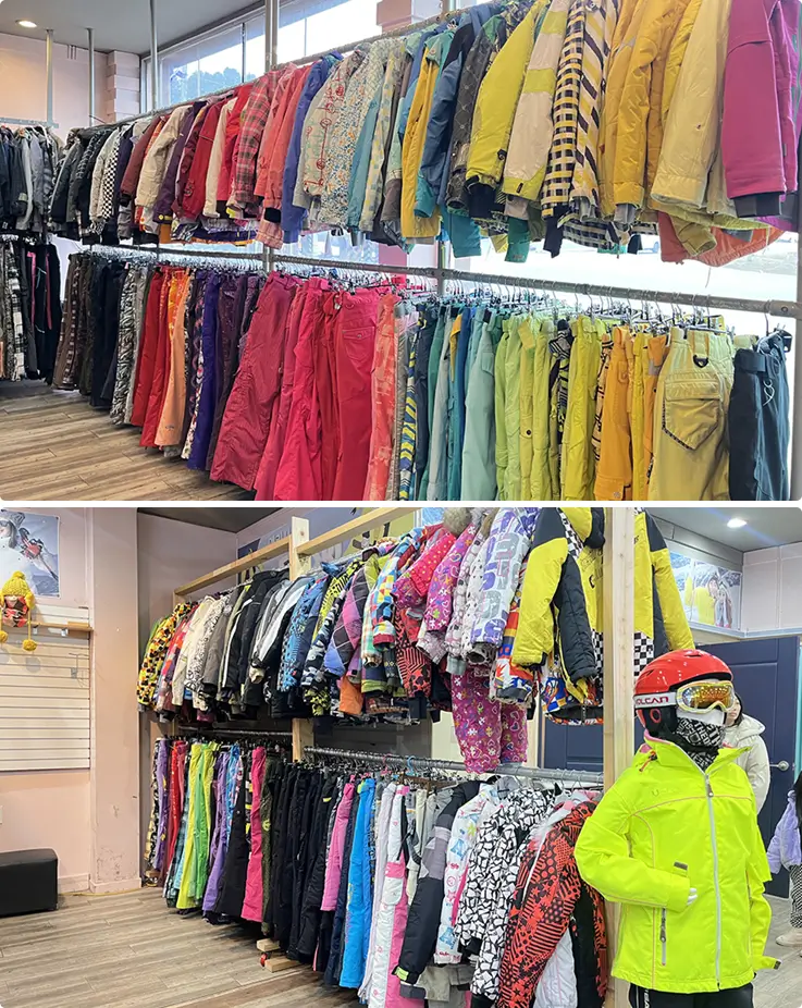 Colorful ski jacets and pants neatly hung in a row at a ski rental shop.