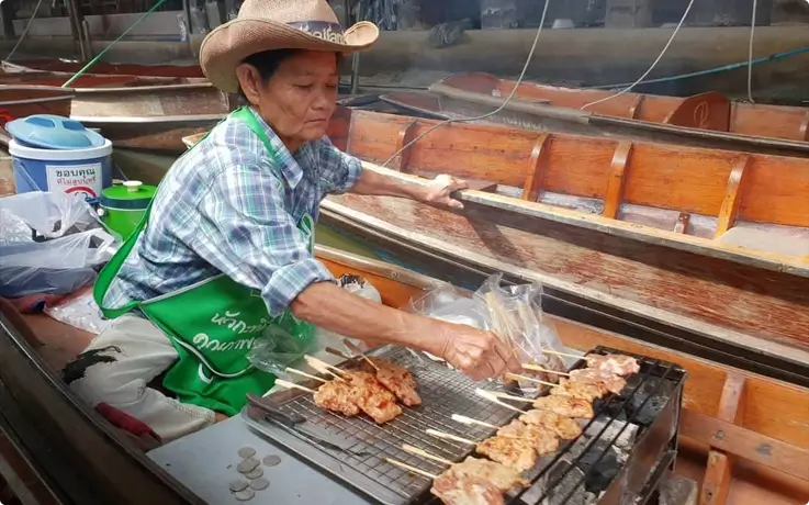 Vendor selling local Thai street food on a wooden boat in Damnoen Saduak