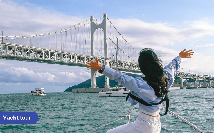 Visitor taking photos on a yacht ride in Busan with Gwangan Bridge in the background
