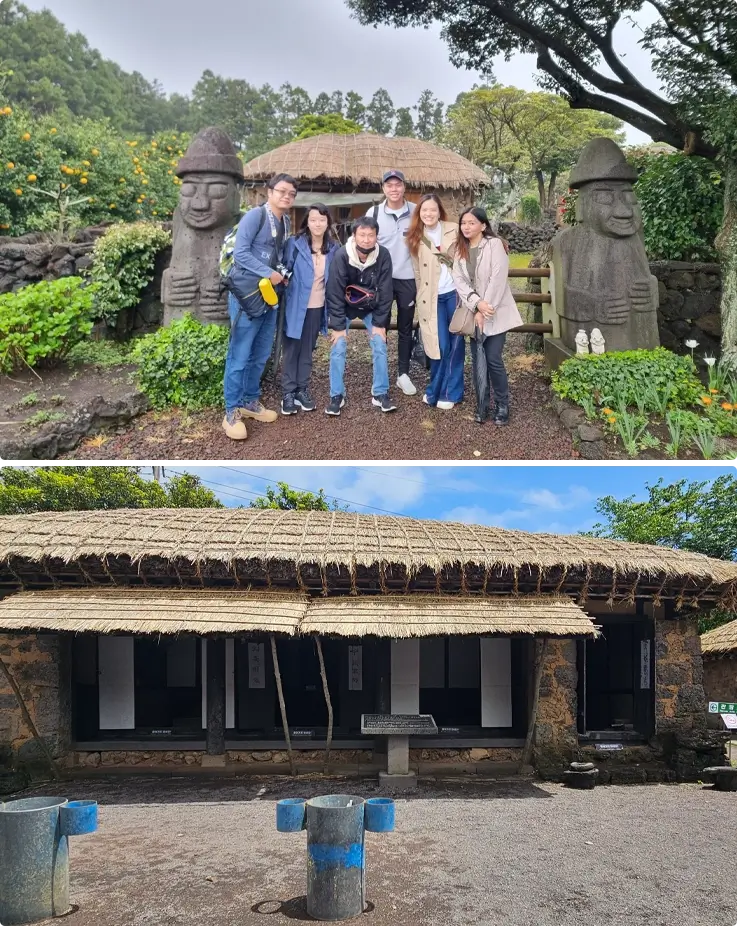 Visitors taking photos in front of a fence with Dolhareubang and a thatched house at Seongeup Folk Village on Jeju Island