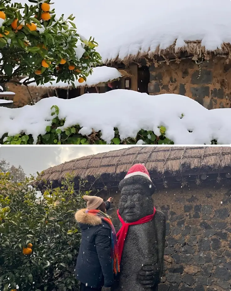 Traditional thatched houses covered in snow at the top and a visitor taking a photo with a Dolhareubang statue at the bottom in Seongeup Folk Village on Jeju Island