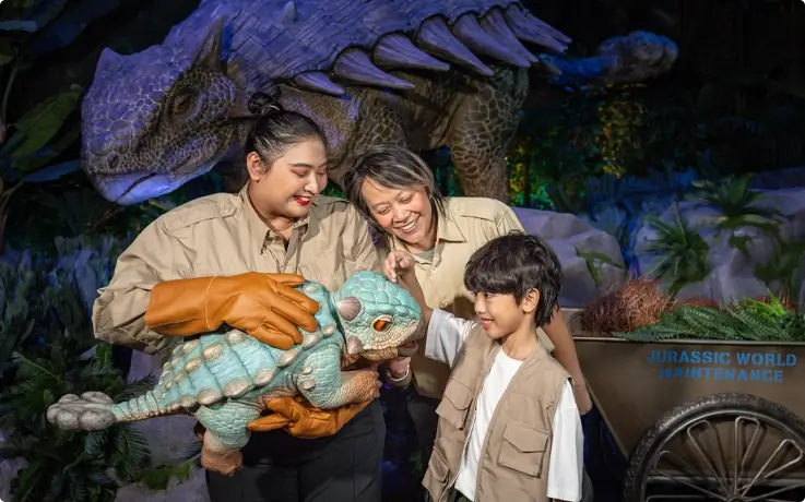 Visitor petting baby dinosaur with the assistance of staff at Jurassic World: The Experience in Bangkok