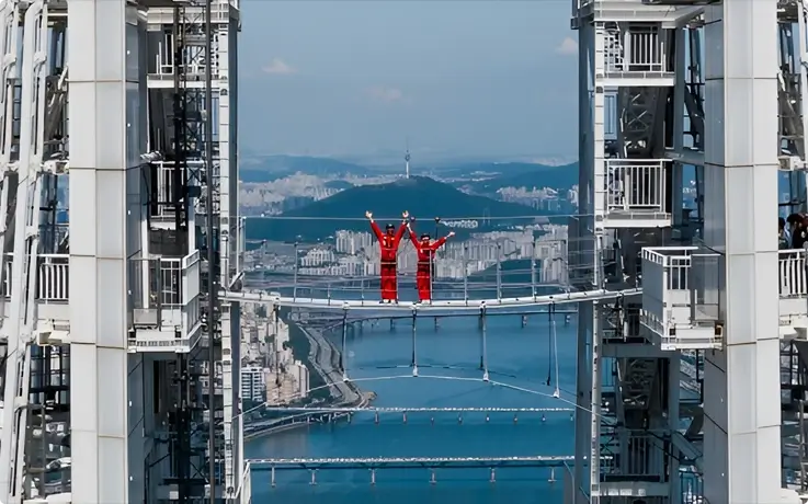 Visitors posing on the Sky Bridge at Lotte World Tower in Seoul with a view of N Seoul Tower in the distance