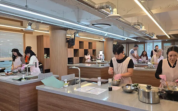 Participants in aprons preparing traditional Korean temple dishes in a modern kitchen.