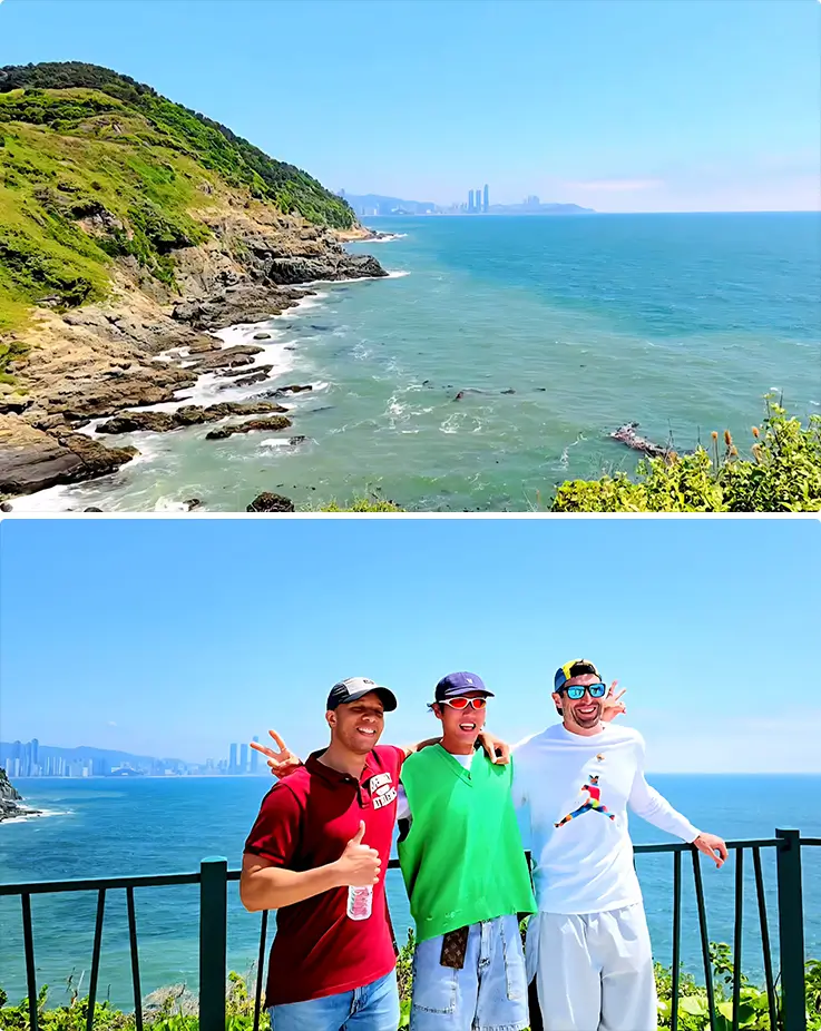 Lush green coastal cliffs line the turquoise sea, with three smiling visitors posing at a scenic Busan oceanfront viewpoint.