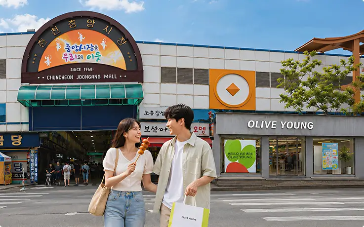A couple strolls past Chuncheon Jungang Market, snacking on skewers near a bustling shopping district.
