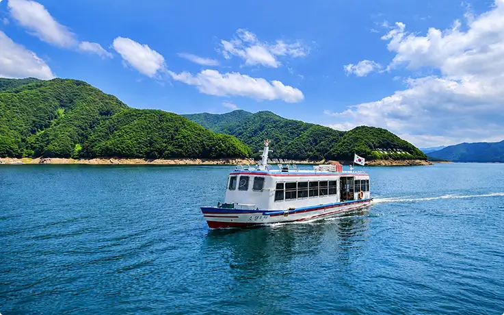 Passenger boat cruising Soyangho Lake reservoir surrounded by peaceful, scenic green mountains.