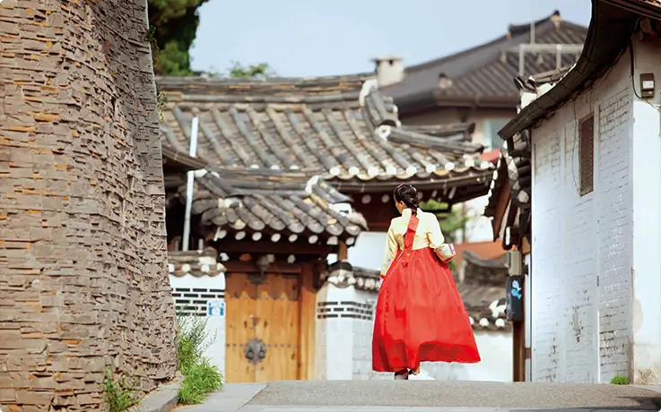 Traditional hanok village alley featuring a woman in vibrant red hanbok strolling gracefully.
