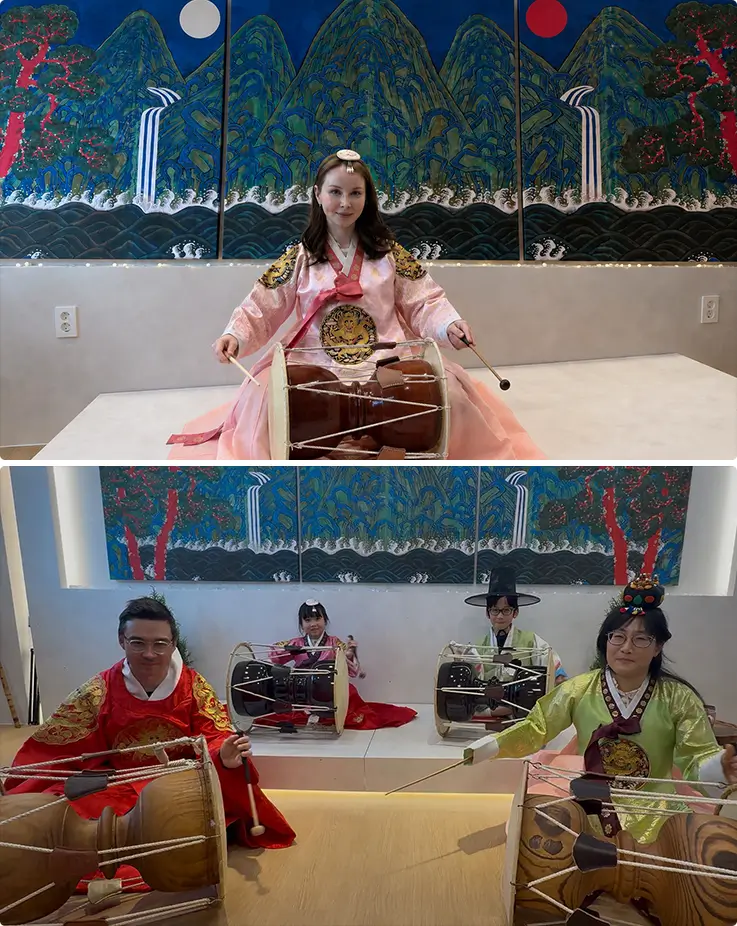 Guests in colorful hanbok playing janggu drums together on traditional stage.