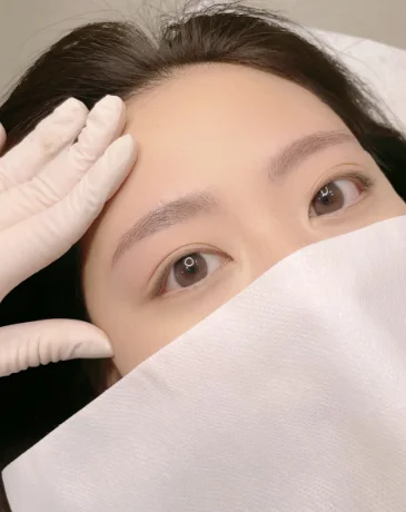 Client resting during Korean eyebrow PMU, showing soft, balanced, naturally defined brows.