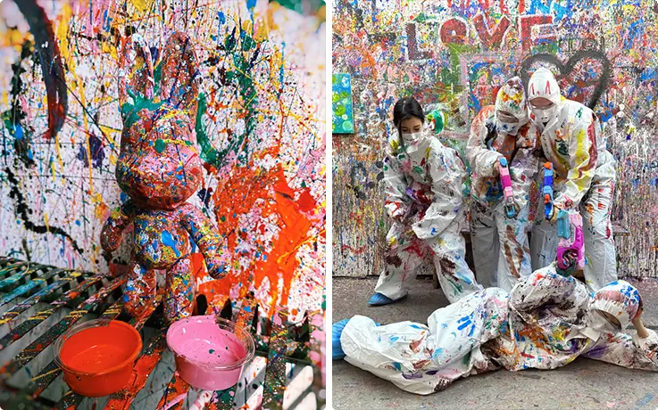 Splatter-painted rabbit figure sits beside vibrant paint bowls on canvas.
