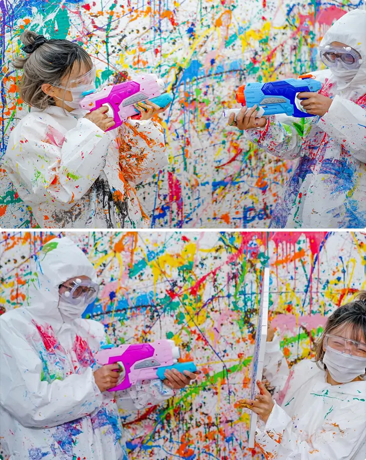 Protective-suited participants blast colorful paint using water guns playfully.