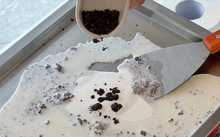 Drizzling chocolate cookie crumbles over a creamy frozen base on a chilled griddle.