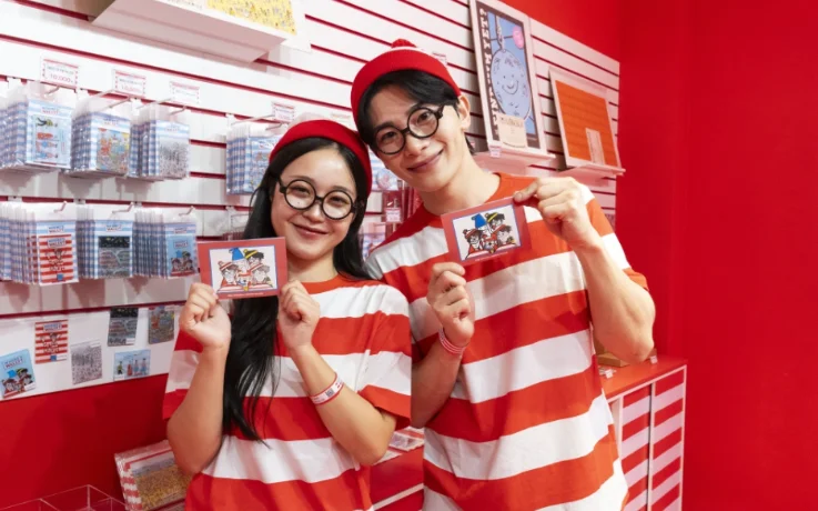 Couple dressed as Wally holds character cards in the Where’s Wally? shop.