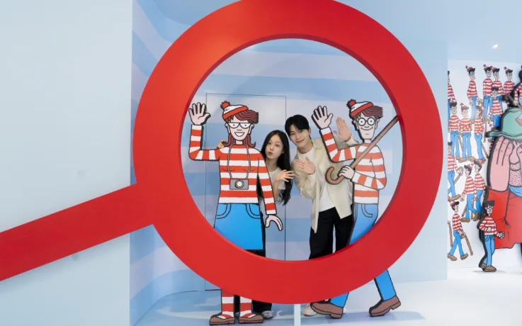 Couple poses inside a giant magnifying glass with Wally and Wenda cutouts.