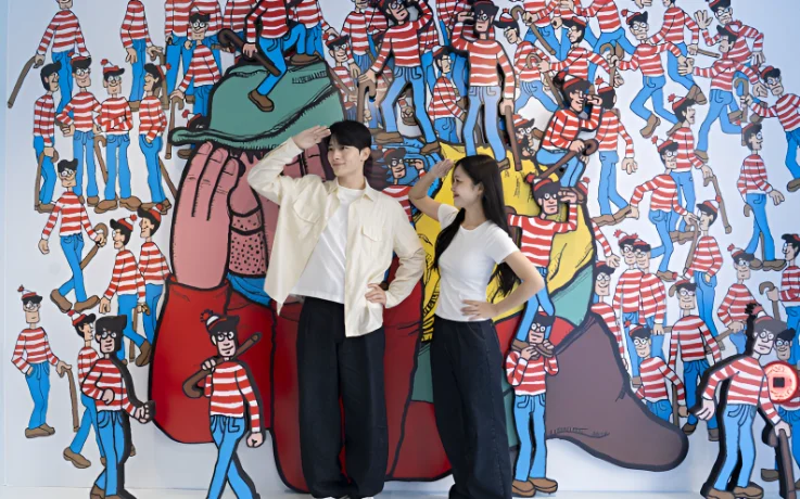Couple strikes searching poses in front of a Where’s Wally? character mural.