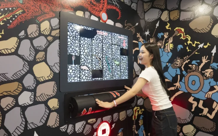 Smiling visitor rolls the interactive controller to play a dragon-themed arcade mission.