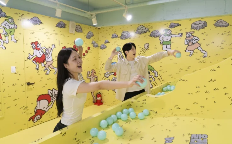 Couple throws balls in a bright yellow Where’s Wally? themed game room.