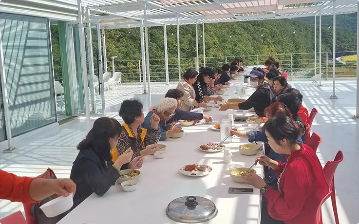 Group enjoying a Korean meal together on a scenic open-air terrace surrounded by nature.