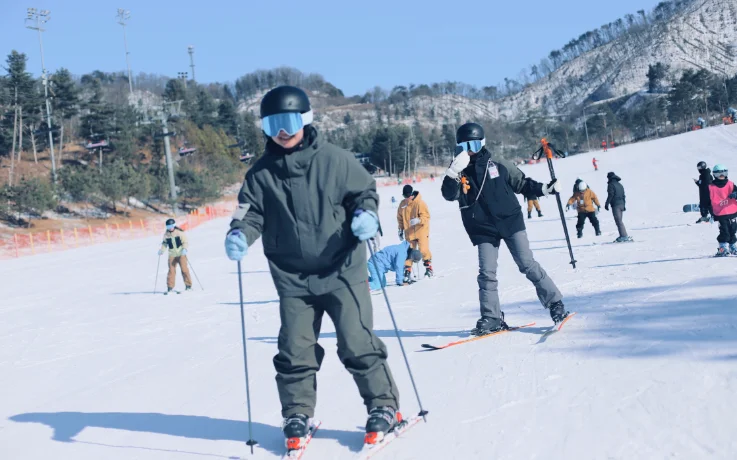 Beginner skier smiling on a gentle Oak Valley slope while an instructor films nearby.