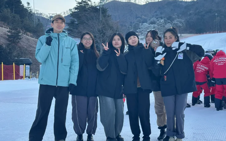 Oak Valley Ski School team posing together on a groomed beginner slope with snowy mountains behind.