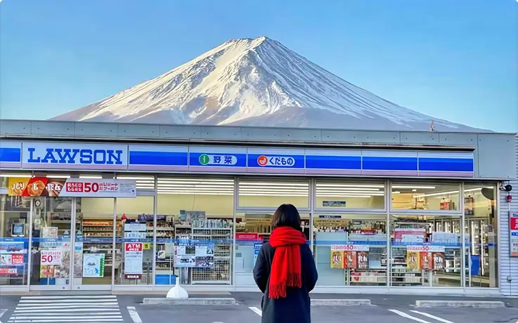 A person posing for photos with Mt. Fuji in the background at Lawson Kawaguchiko Station in Yamanashi