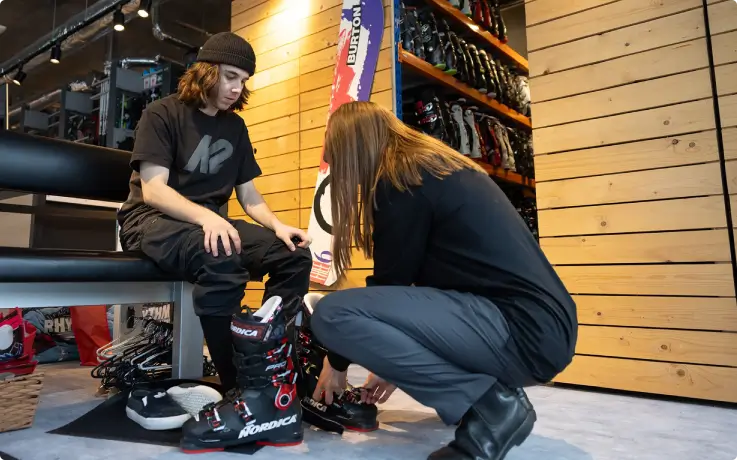Friendly store clerk helping a customer try on ski boots at a ski rental store.
