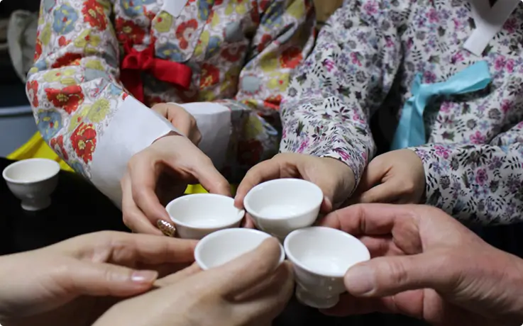Hands holding small white cups, toasting with traditional Korean tea.