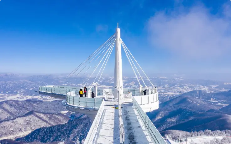 Traveler walking on the Balwangsan Skywalk overlooking snowy mountains.
